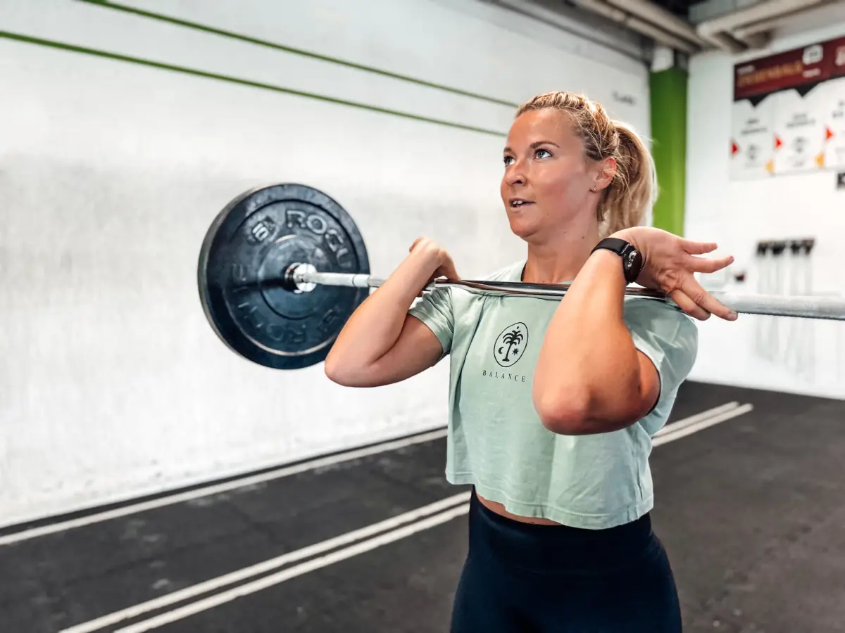 Athlete holding a barbell in the front-rack position in front of a white gym wall