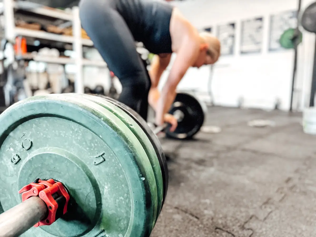 Loaded barbell in the foreground with an athlete deadlifting in the background