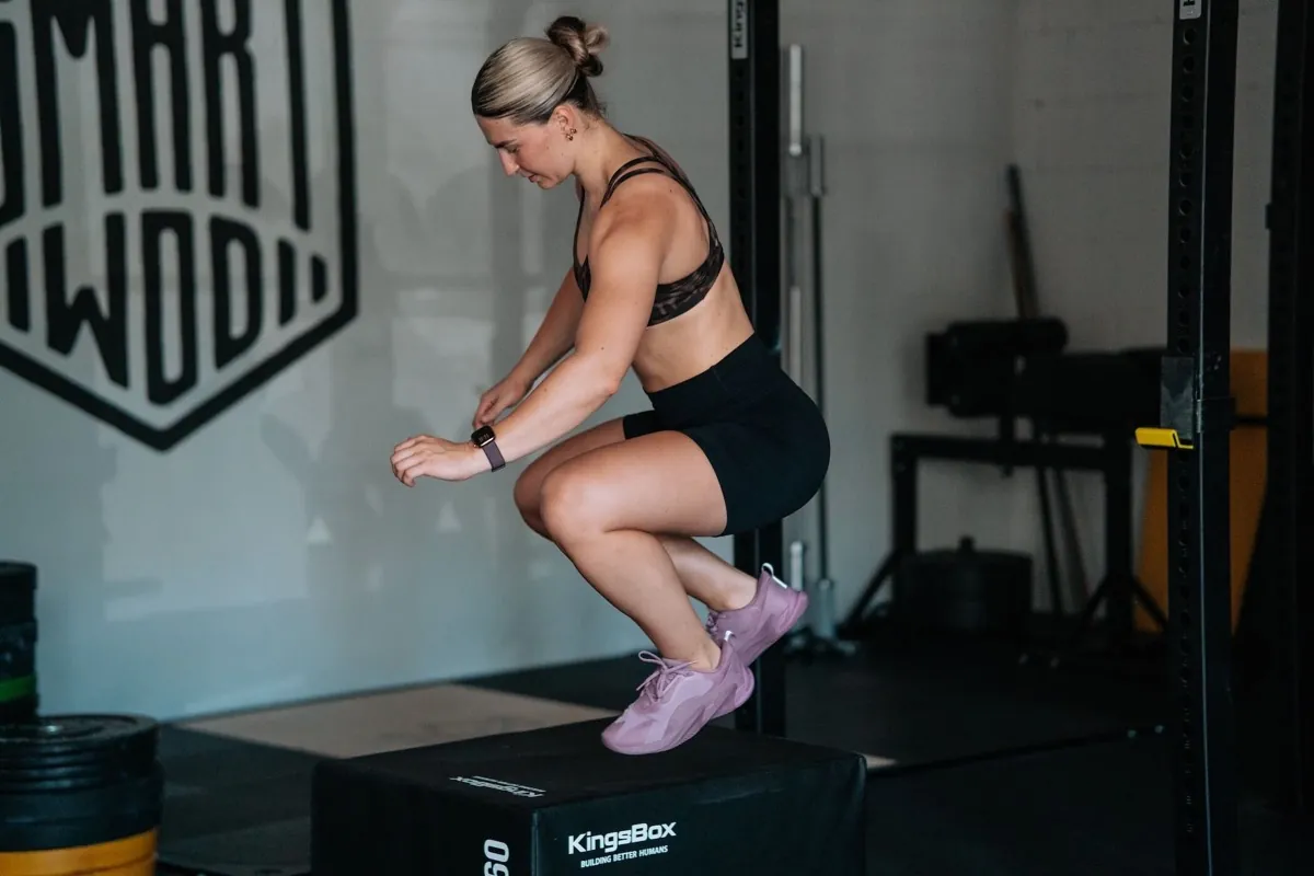 Athletin landet einen Box Jump vor dem SmartWOD-Logo