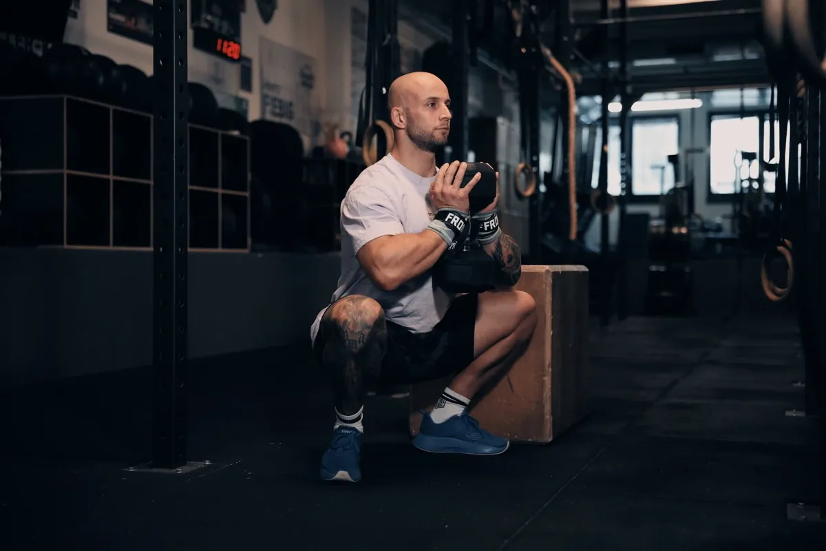 Athlet macht einen Goblet Squat auf eine Box in einem dunklen Gym
