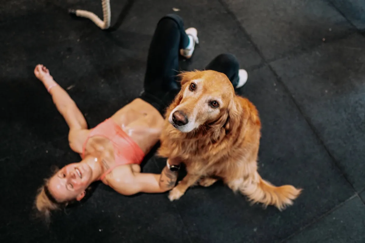 Erschöpfte, glückliche Athletin liegt nach dem Workout am Boden neben einem Hund