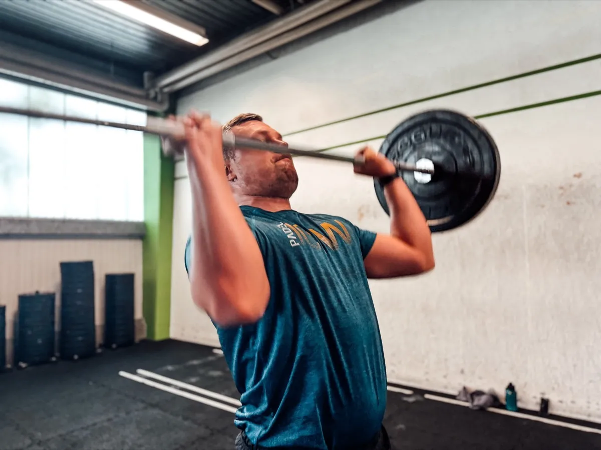 Athlet drückt die Langhantel beim Push Press über Kopf