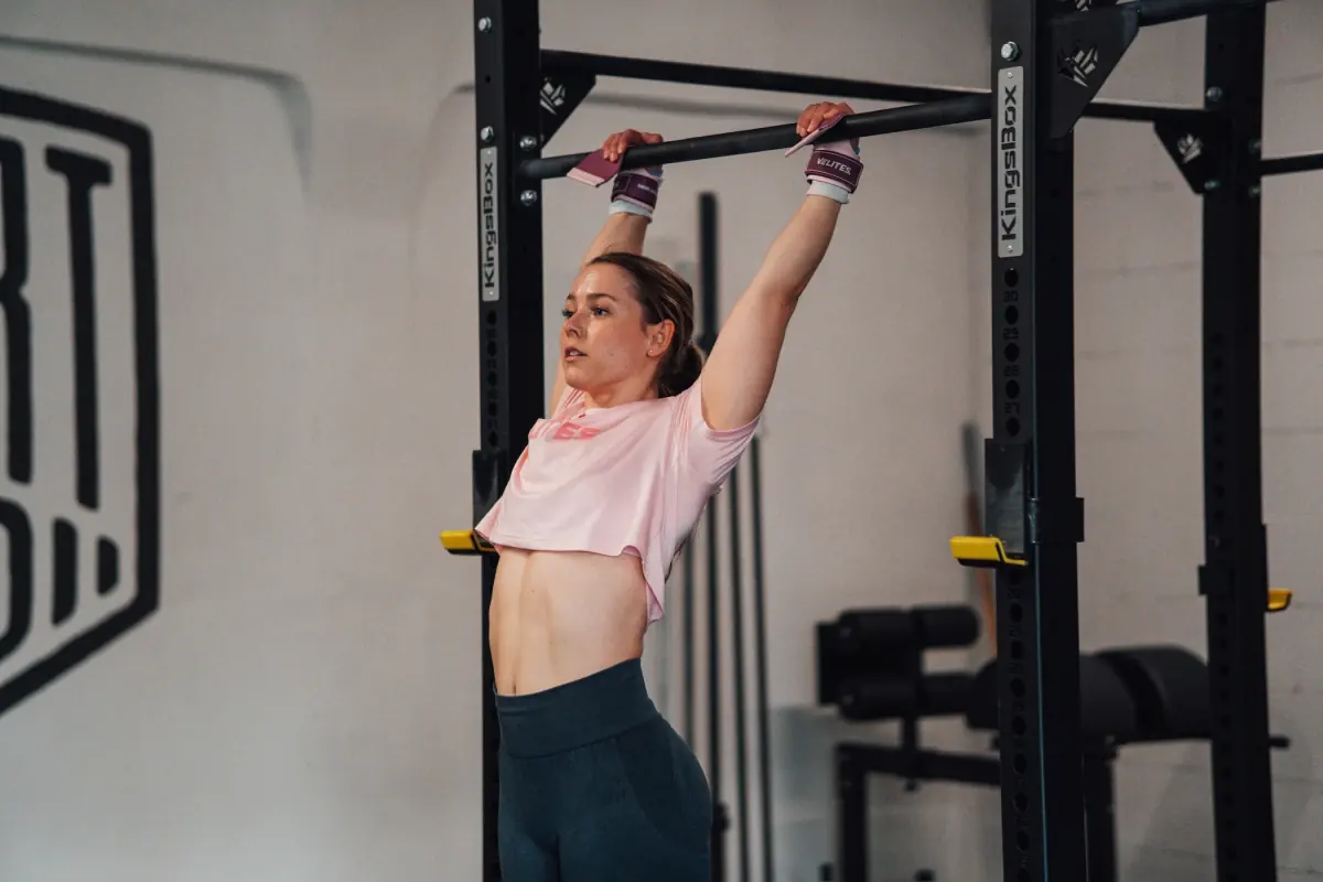 Athletin hängt mit Handgelenkbandagen an der Pull-up-Stange und spannt die Körpermitte an