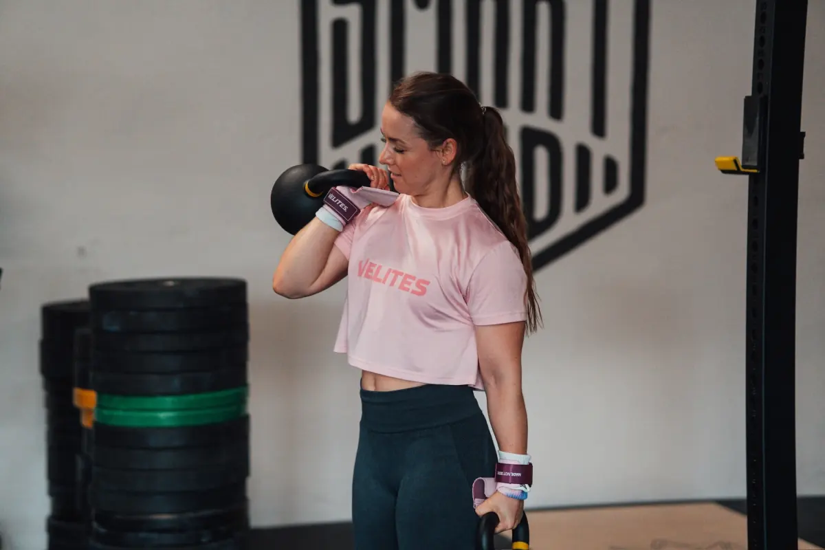 Athletin hält eine Kettlebell in der Front-Rack-Position und eine zweite am gestreckten Arm