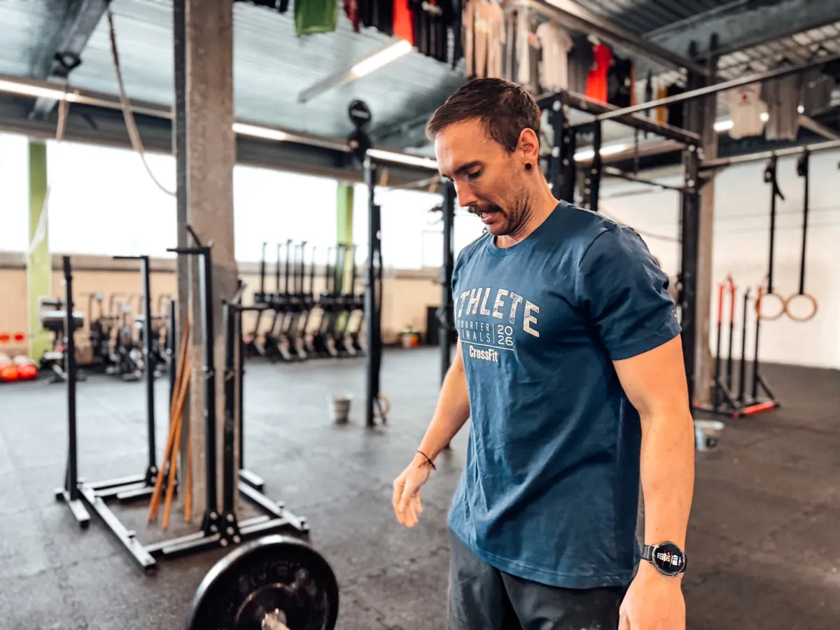 Athlete standing next to a barbell in a CrossFit box, catching a breath between sets
