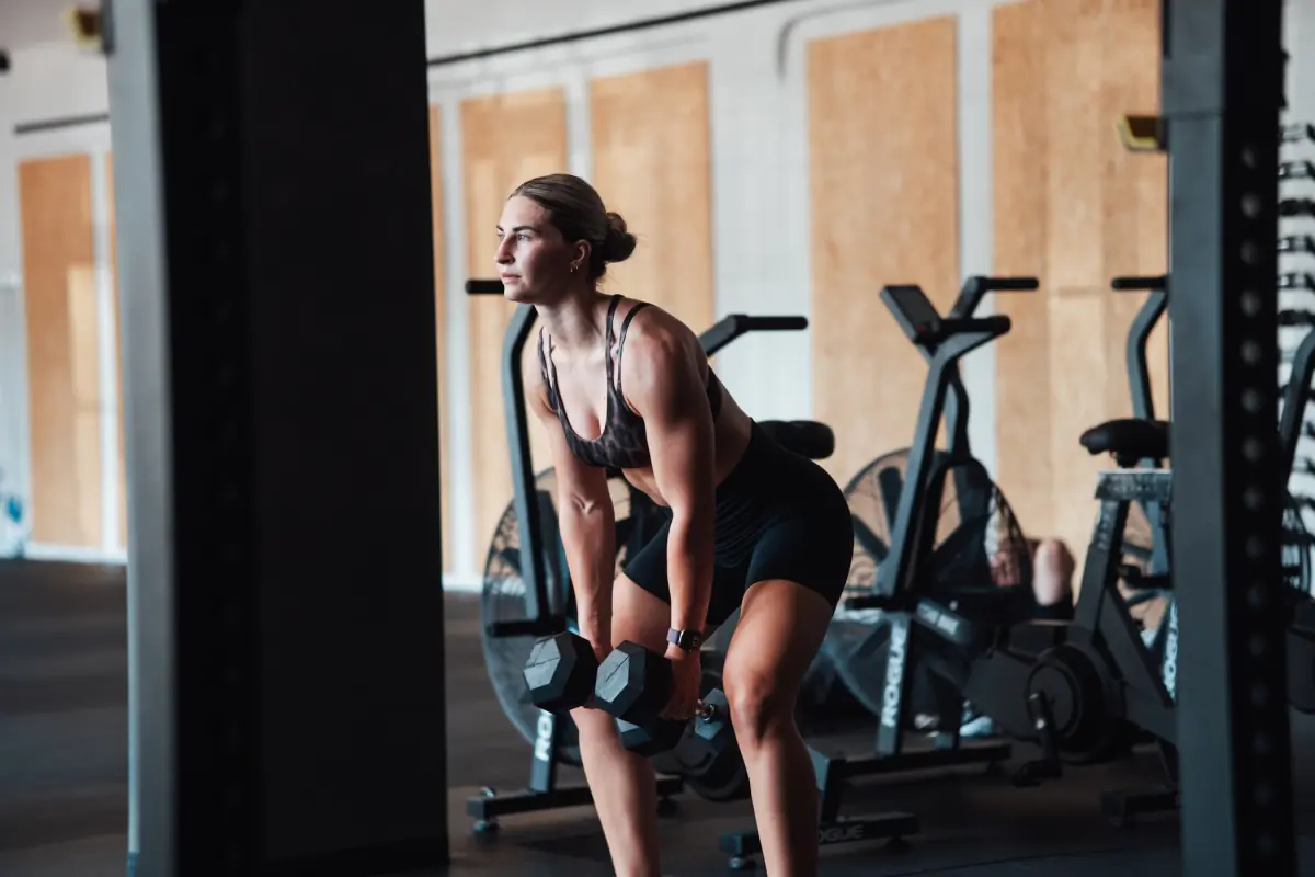Athlete in a hip hinge holding two dumbbells in front of a row of air bikes