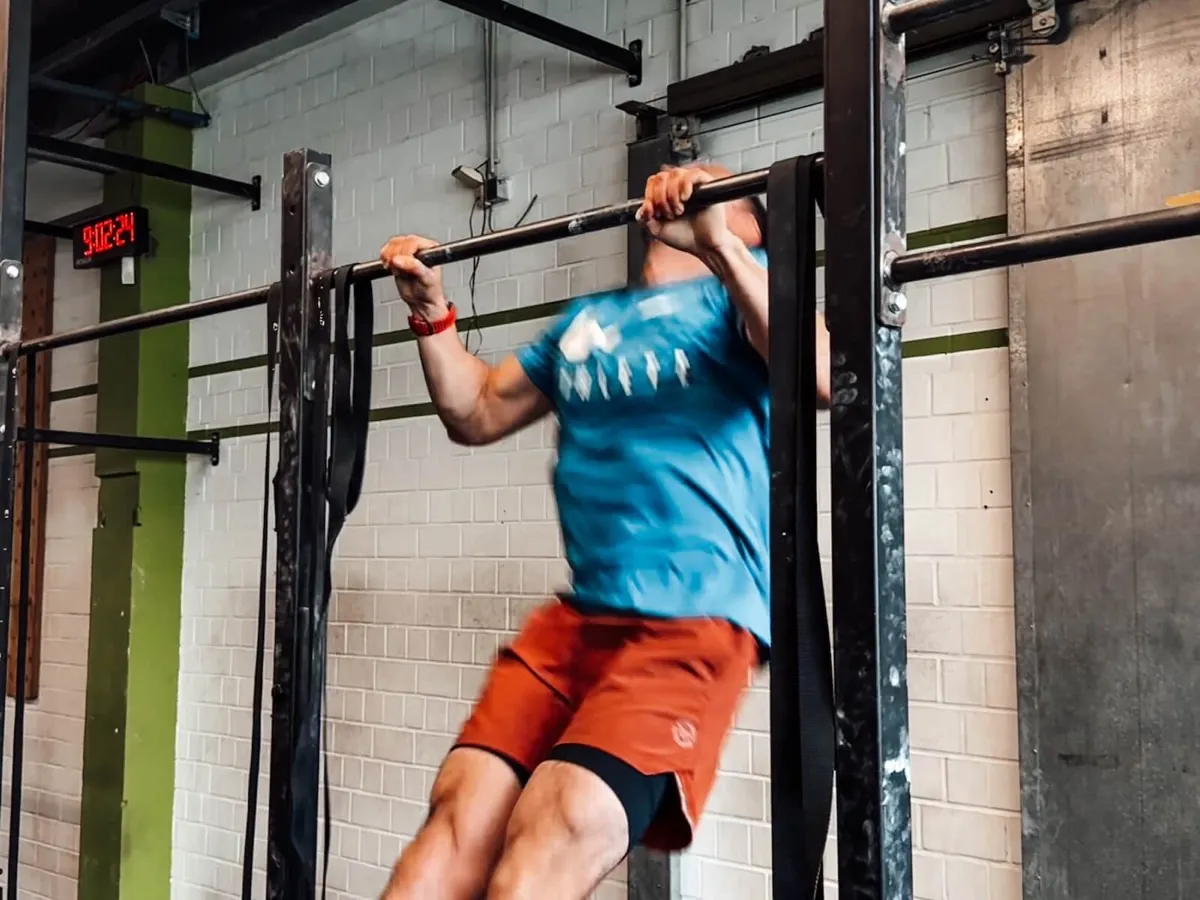 Athlet bei Kipping Pull-ups an der Stange in einer CrossFit-Box
