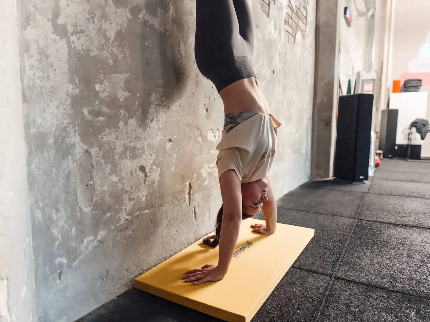 Athletin im Handstand an der Wand auf einer gelben Matte