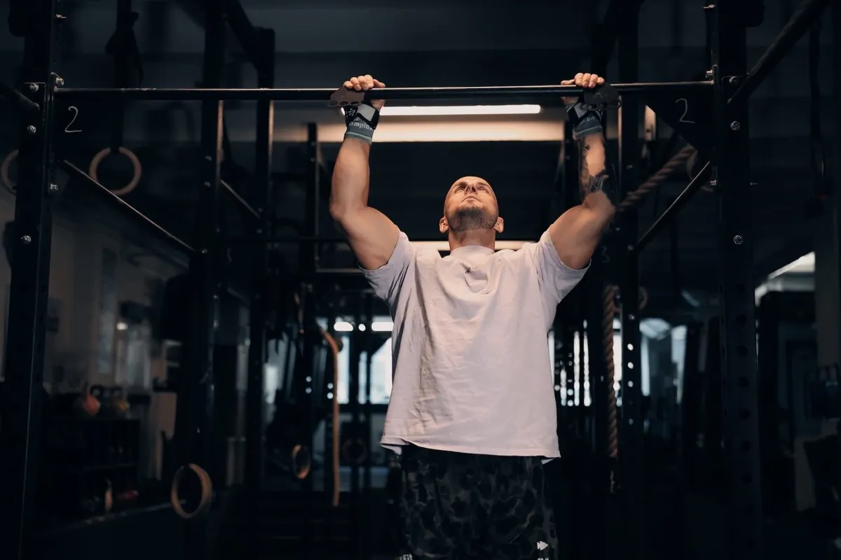Athlet hängt im Dead Hang an der Klimmzugstange in einem dunklen Gym